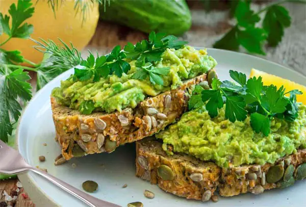 Thick slices of stacked avocado toast on whole grain bread.