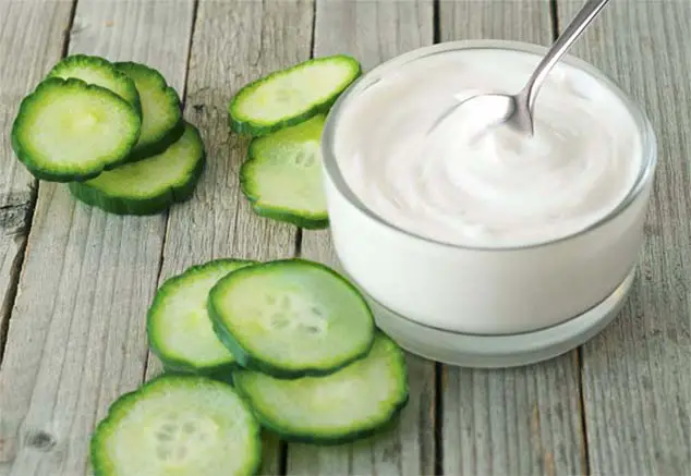 Jar of rich cucumber facial mask cream alongside cucumber slices on a wooden board.