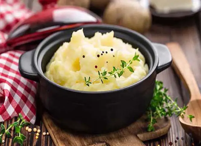 Rich and fluffy bowl of homemade mashed potatoes with garlic and herbs.