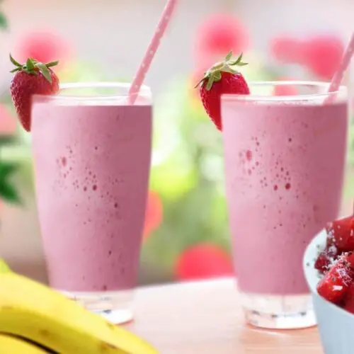 Two tall glasses of homemade smoothies by fresh fruit present this strawberry banana smoothie recipe.