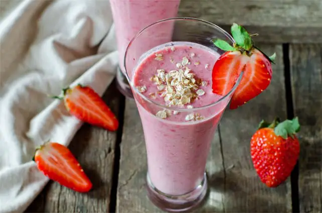 Rich and creamy vegan strawberry smoothie in a tall glass topped with oats and fresh sliced strawberry.