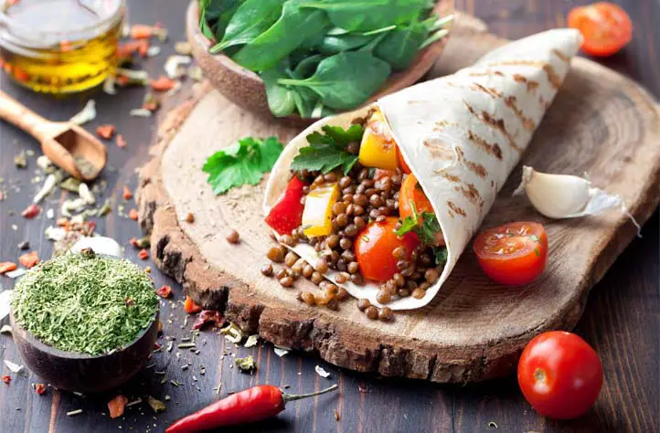 Delicious stuffed vegan wrap with legumes, veggies, and herbs on a cutting board.