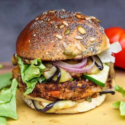 Close-up of a delicious vegan black bean burger that's 100% stacked by a plump beefsteak tomato and organic leafy greens.