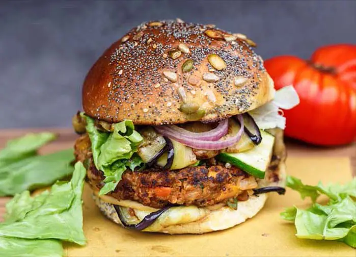 Close-up of a delicious vegan black bean burger that's 100% stacked by a plump beefsteak tomato and organic leafy greens.