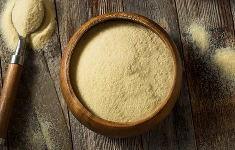 Top view of rich golden nutritional yeast in a bowl and spoon on a rustic board.