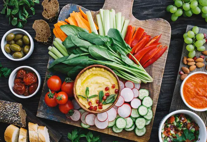 Top view of delicious vegan appetizers and finger foods including veggies and dips on a rustic cutting board.