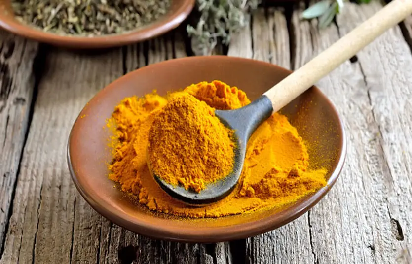 Bowl and heaping spoonful of turmeric powder on a rustic wood. 