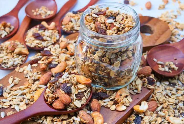 Huge jar and spoons of loaded homemade granola on a board.