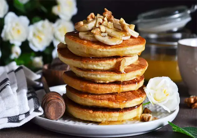 Towering stack of delicious vegan pancakes with fruit and syrup.