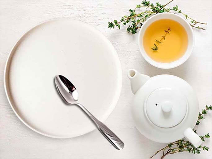 An empty plate and spoon beside a cup of tea present the benefits of fasting.