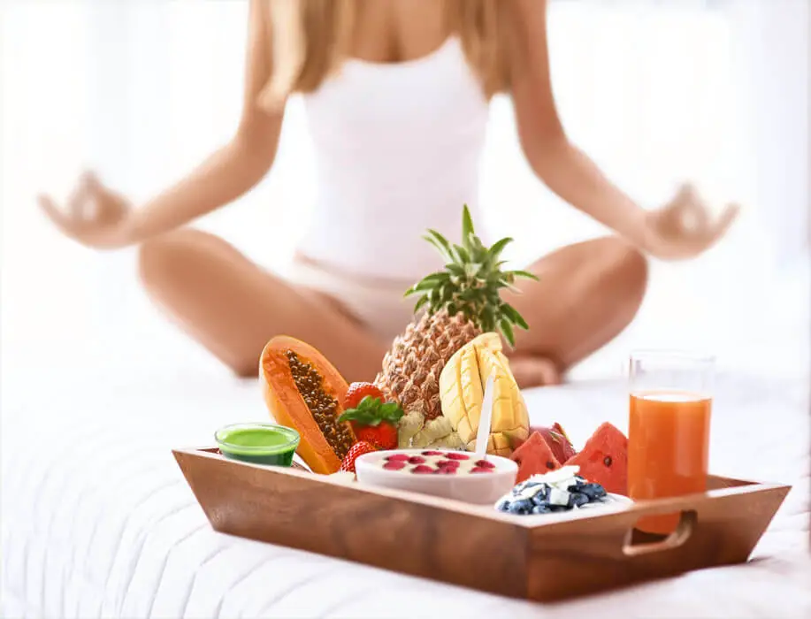 Girl in yoga posture by tray of healthy raw foods.