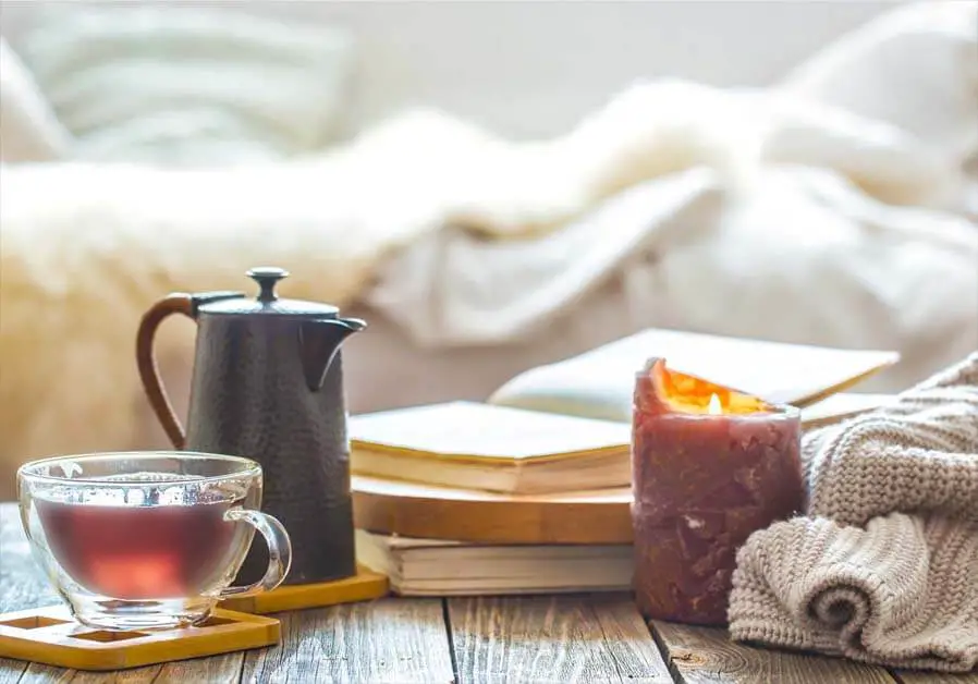 A candlelit nightstand with a cup of tea and stack of books. 