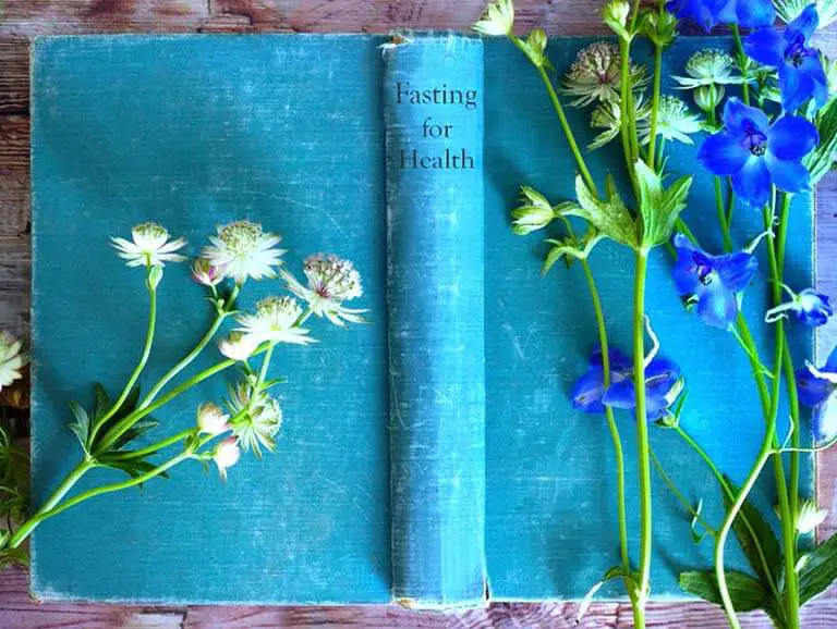 A vintage 'Fasting for Health' book and flowers on a rustic board. 