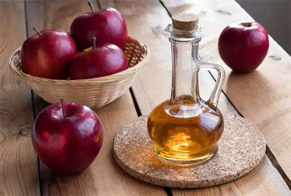 Jug of bright apple cider vinegar on a wooden table by whole Red Delicious apples. 