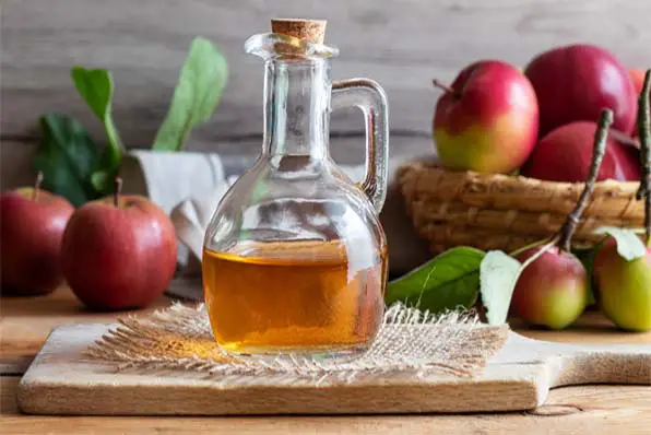 Gorgeous fresh whole apples off the tree behind a jug of rich apple cider vinegar on a cutting block. 