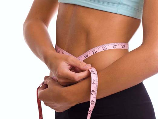 Close-up of a girl's midriff as she  measures her waistline. 