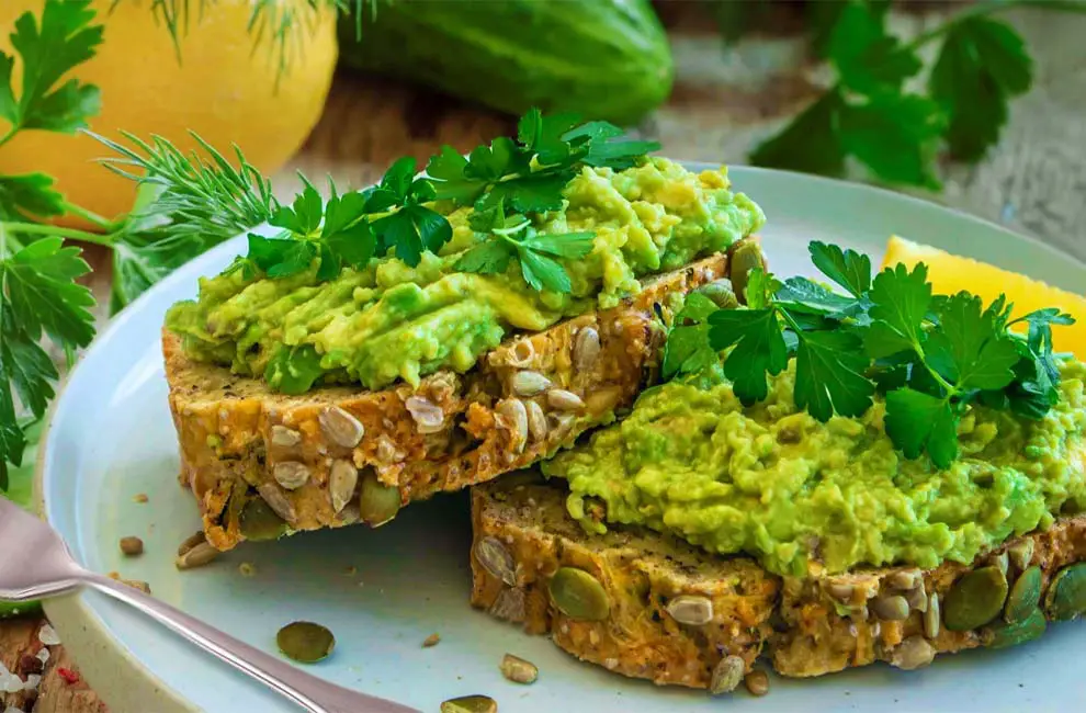 Close-up of succulently rich slices of avocado toast topped with fresh green herbs on homemade sourdough bread.   