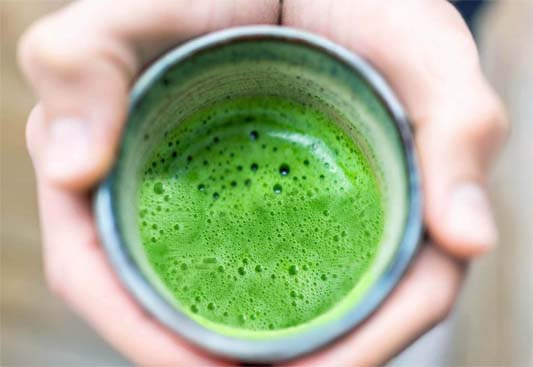 Close-up of hands cupping a rich green shot of barley grass juice.  