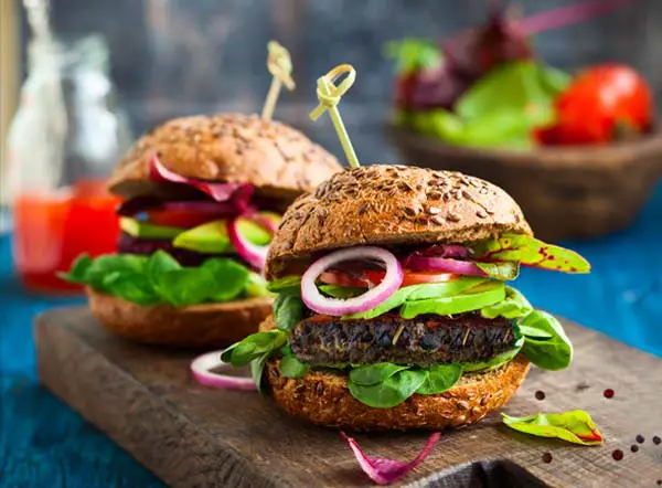 Two loaded black bean burgers on a tabletop wood block. 