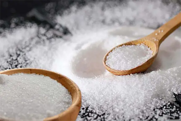 A black board stacked with wooden spoons and glistening piles of bright Epsom salt crystals.