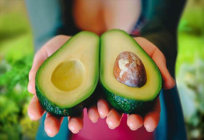 Girl holding up a sliced avocado. 