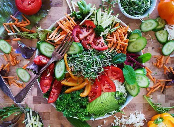 Top view of huge mixed green salad with veggies, sprouts, seeds, and more.