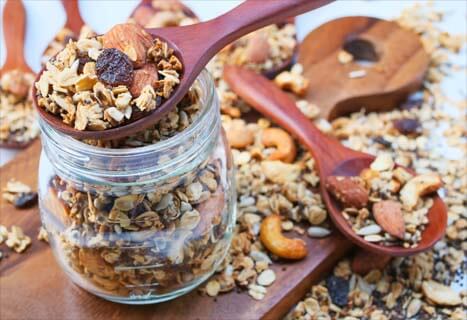 Open jar and heaping spoons of homemade granola. 