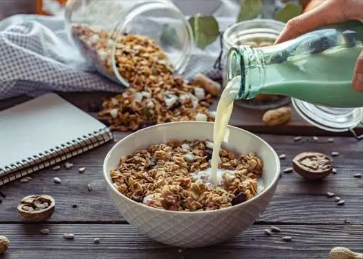 A person pouring plant milk on a bowl of homemade granola. 