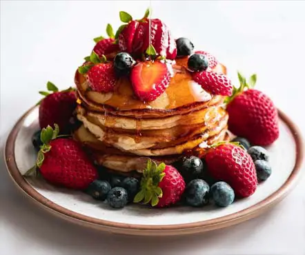 Stack of homemade pancakes covered with fruit and syrup. 