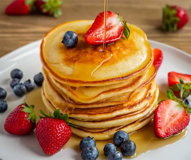 Stack of delicious vegan pancakes with fruit and syrup.