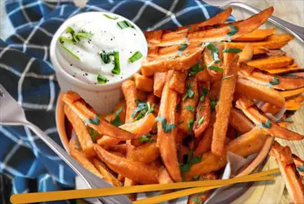 Close-up of succulent sweet potato fries and Ranch topped with green onions and organic chives. 