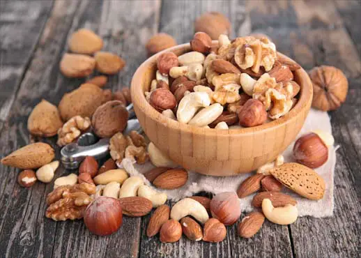 Overflowing wooden bowl of delicious mixed nuts on a rustic board with whole walnuts and a nutcracker. 