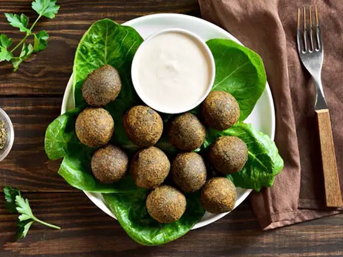 Top view of crispy baked falafel balls on a leafy plate with vegan Ranch dip and healthy herbs.