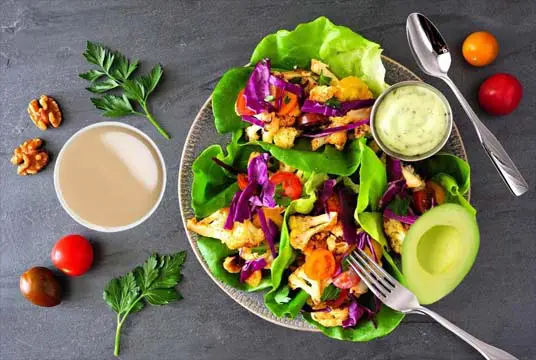 Tops view of heavily stacked lettuce wraps on a plate with dips, fresh avocado, cherry tomatoes, walnuts, and herbs.  