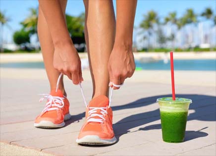 Girl lacing tennis shoes by a cup of wheatgrass. 