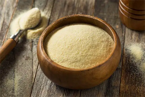 Rustic teakwood bowl and spoonful of nutritional yeast on a rustic board.