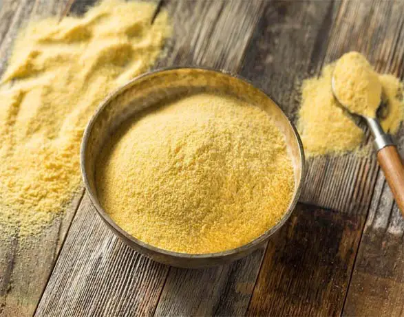 Bowl and overflowing spoonful of nutritional yeast on a planked rustic board.