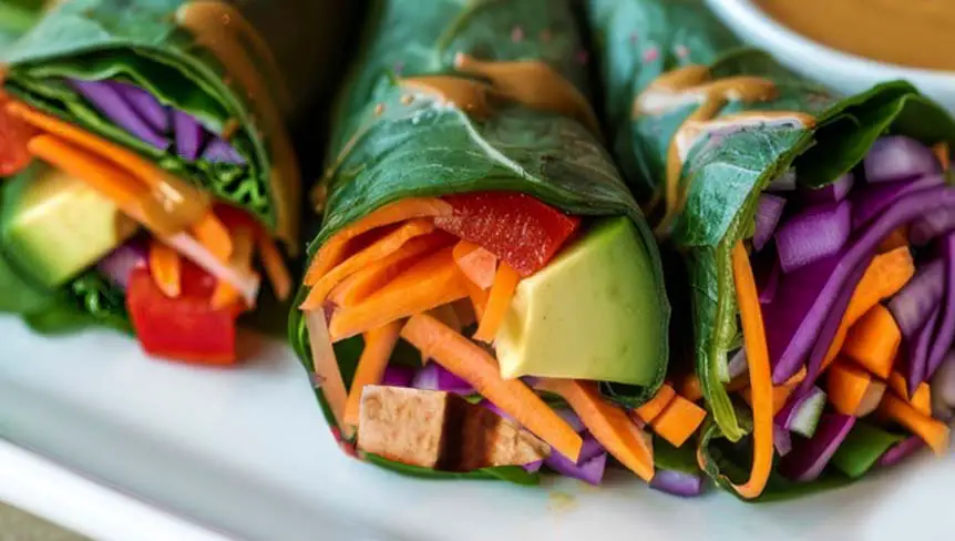 Close-up of three vegan lettuce wraps packed with tofu, veggies, avocado, and a creamy rich peanut sauce. 