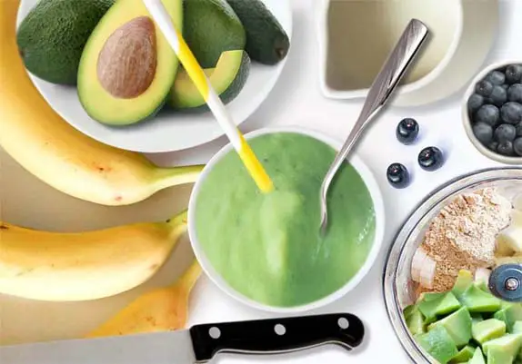 Avocado smoothie recipe in progress with stacked blender and ingredients on a board.