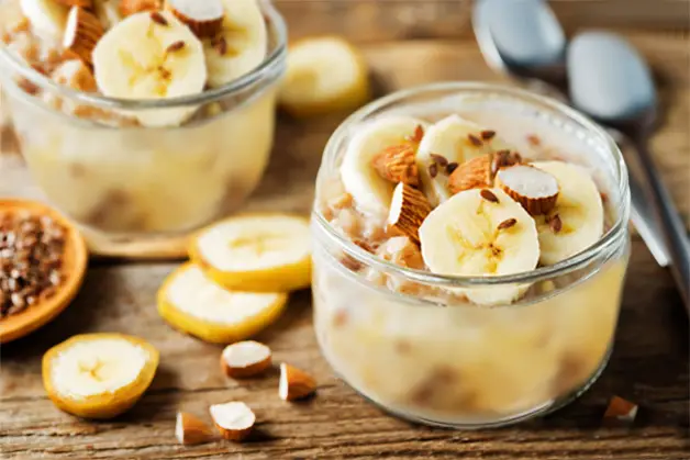 Two banana smoothies stacked with banana slices and nuts.