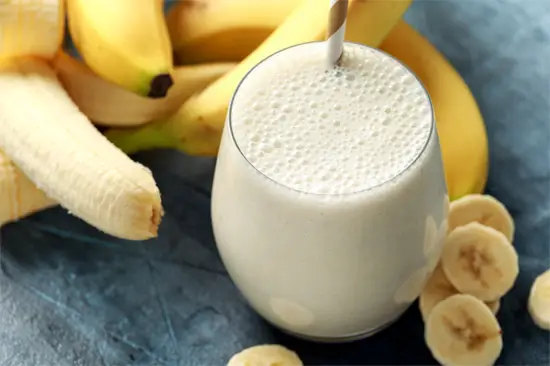 Glass of banana smoothie surrounded by bananas. 