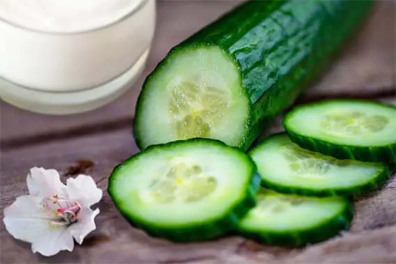 Close-up of cucumber facial cream and sliced fresh cucumber on a rustic board.  