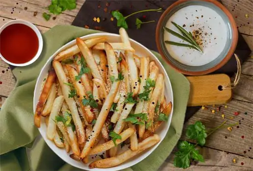 Bowl of homemade French fries with dips on a rustic board. 