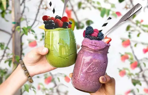 Close on two girls' hands toasting with giant mugs of frozen fruit smoothies.