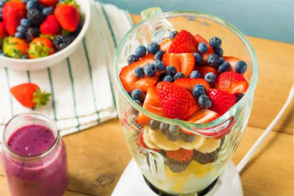 Top view of a blender stacked with fresh fruits including bananas and berries. 