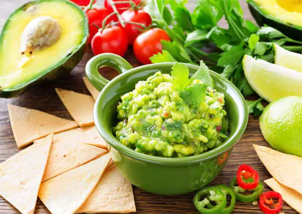 Bowl of homemade guacamole with chips, avocado, tomatoes, cilantro, lemon, and Jalepeno peppers. 