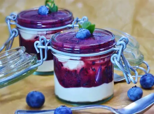 Two stacked mason jars of rich vegan yogurt with fresh organic blueberries and pools of coulis.