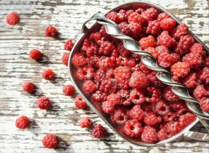 Top view of fresh organic raspberries in a basket on a rustic board. 