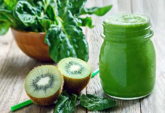 Large jar of spinach smoothie by fresh kiwi and spinach leaves. 