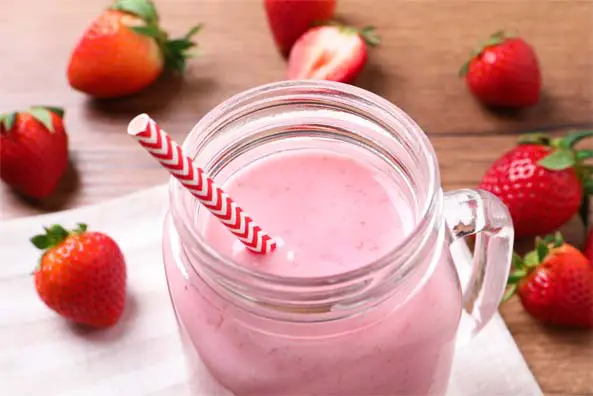 Top view of creamy rich vegan strawberry smoothie in a mason jar glass surrounded by fresh whole strawberries. 